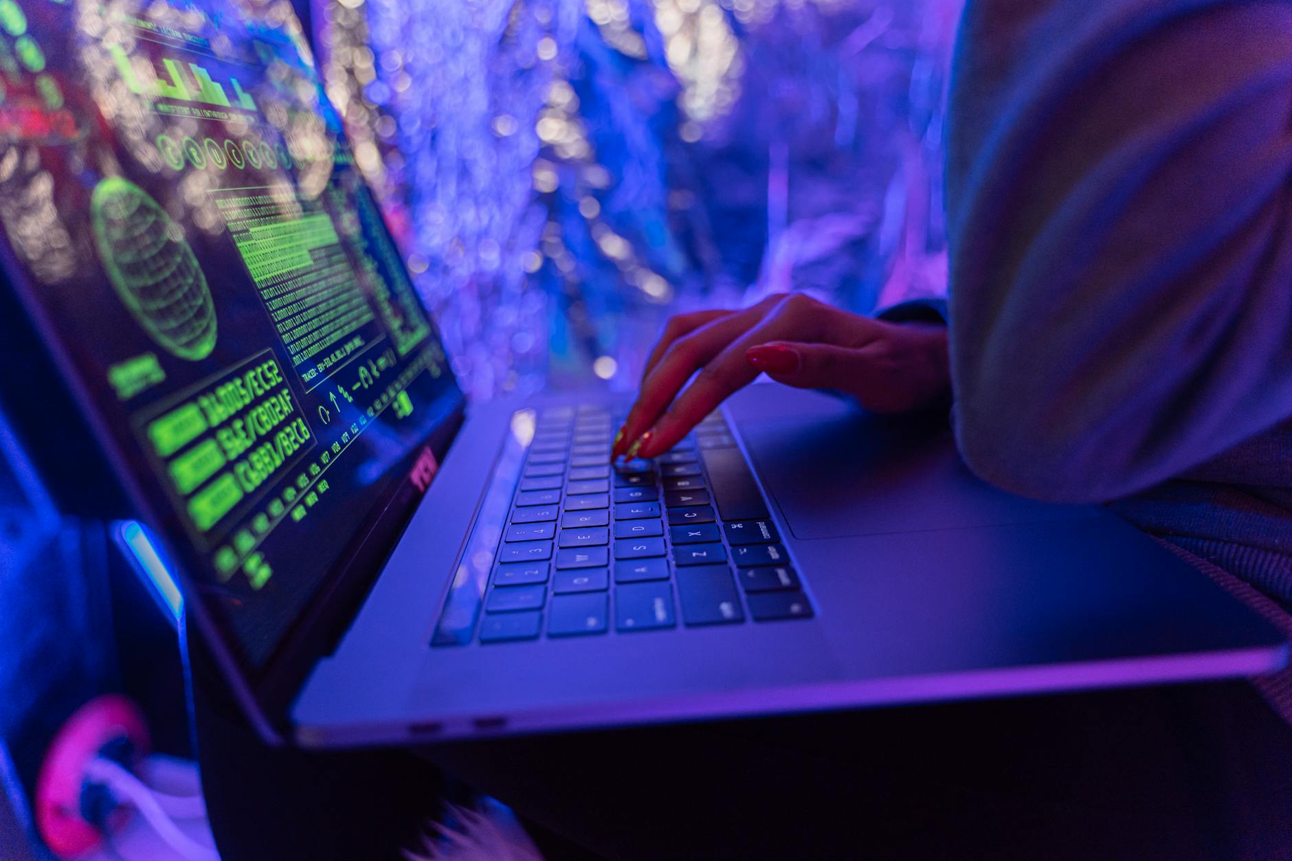 Hands typing on a laptop displaying cybersecurity graphics, illuminated by purple light