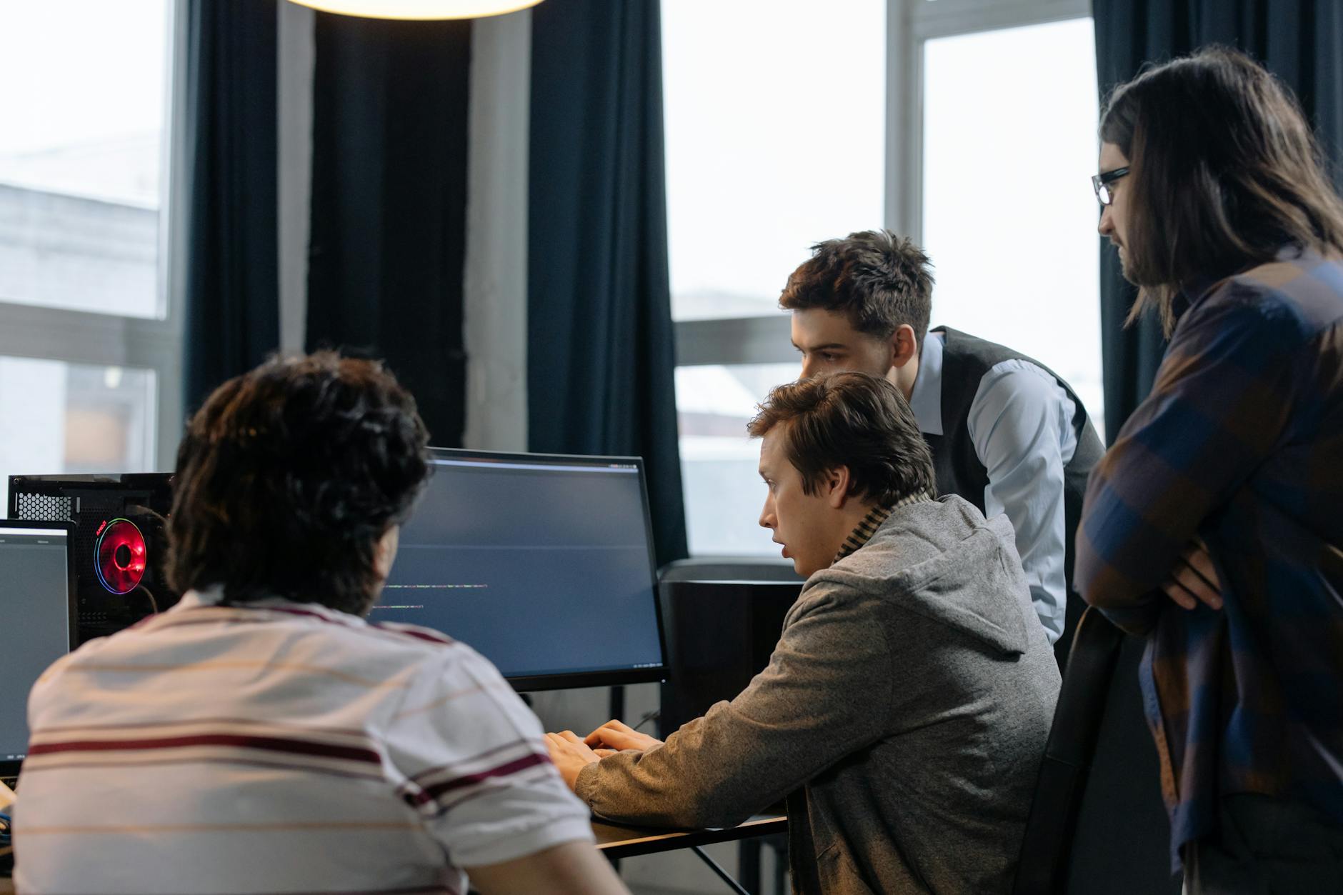 Group of software developers collaborating around computers in a modern open-plan office.
