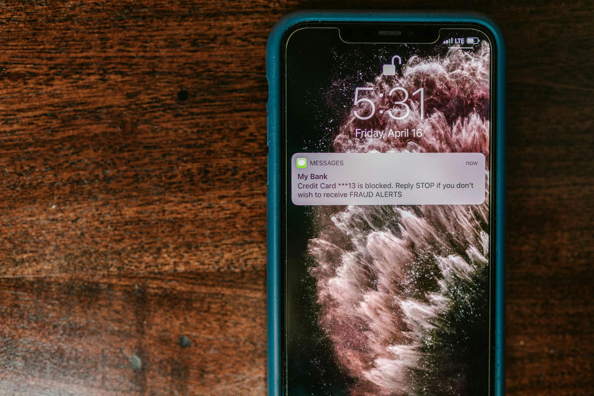 Smartphone displaying fraud alert, on wooden surface