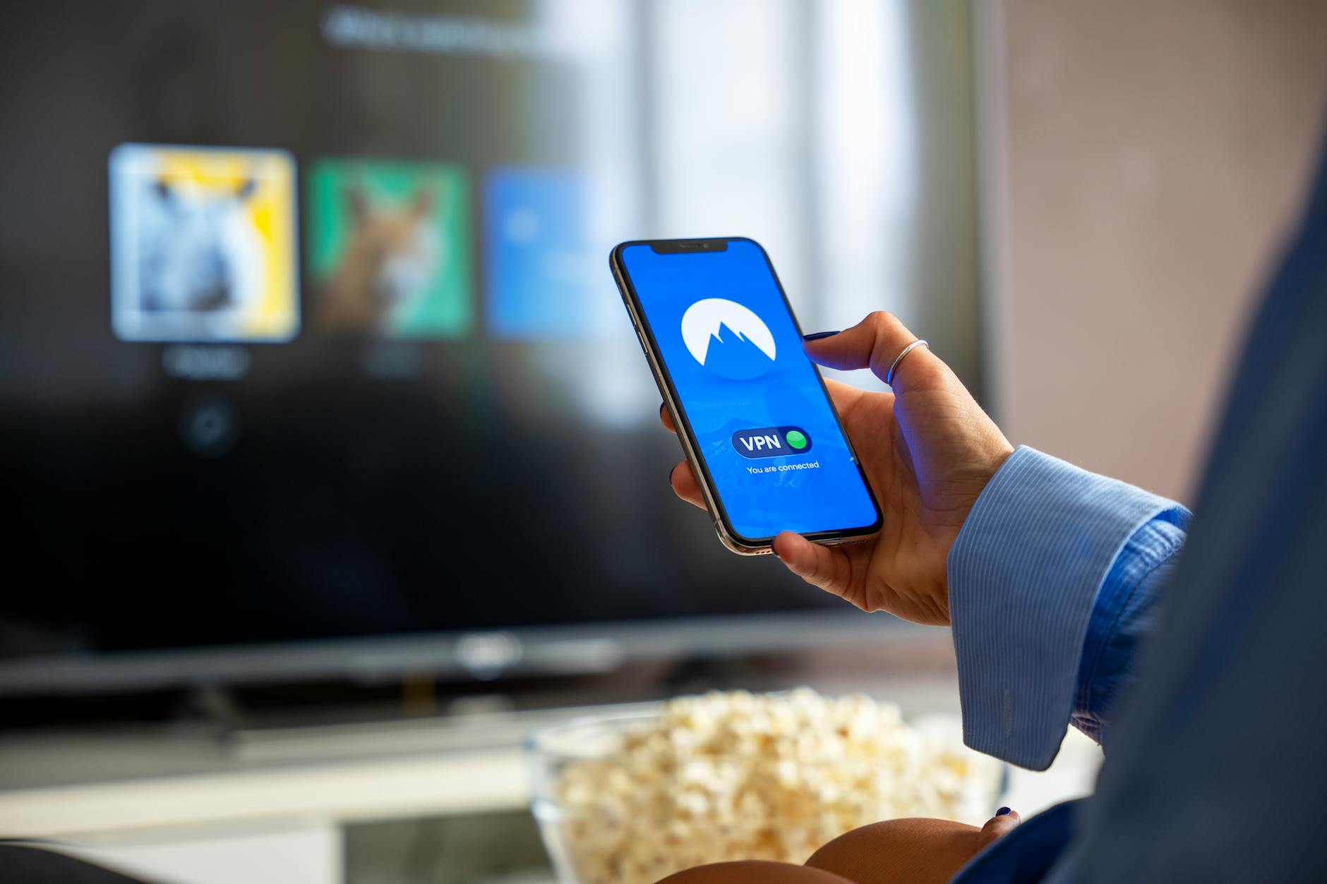 Person using a smartphone while watching a smart TV at home, depicting the connected TV viewing experience