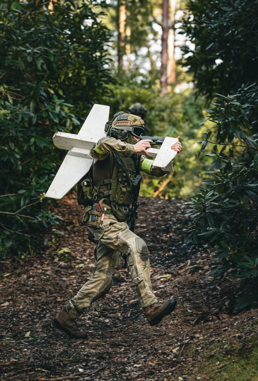 A soldier in camouflage gear carrying a drone in a dense forest setting, demonstrating modern military technology.
