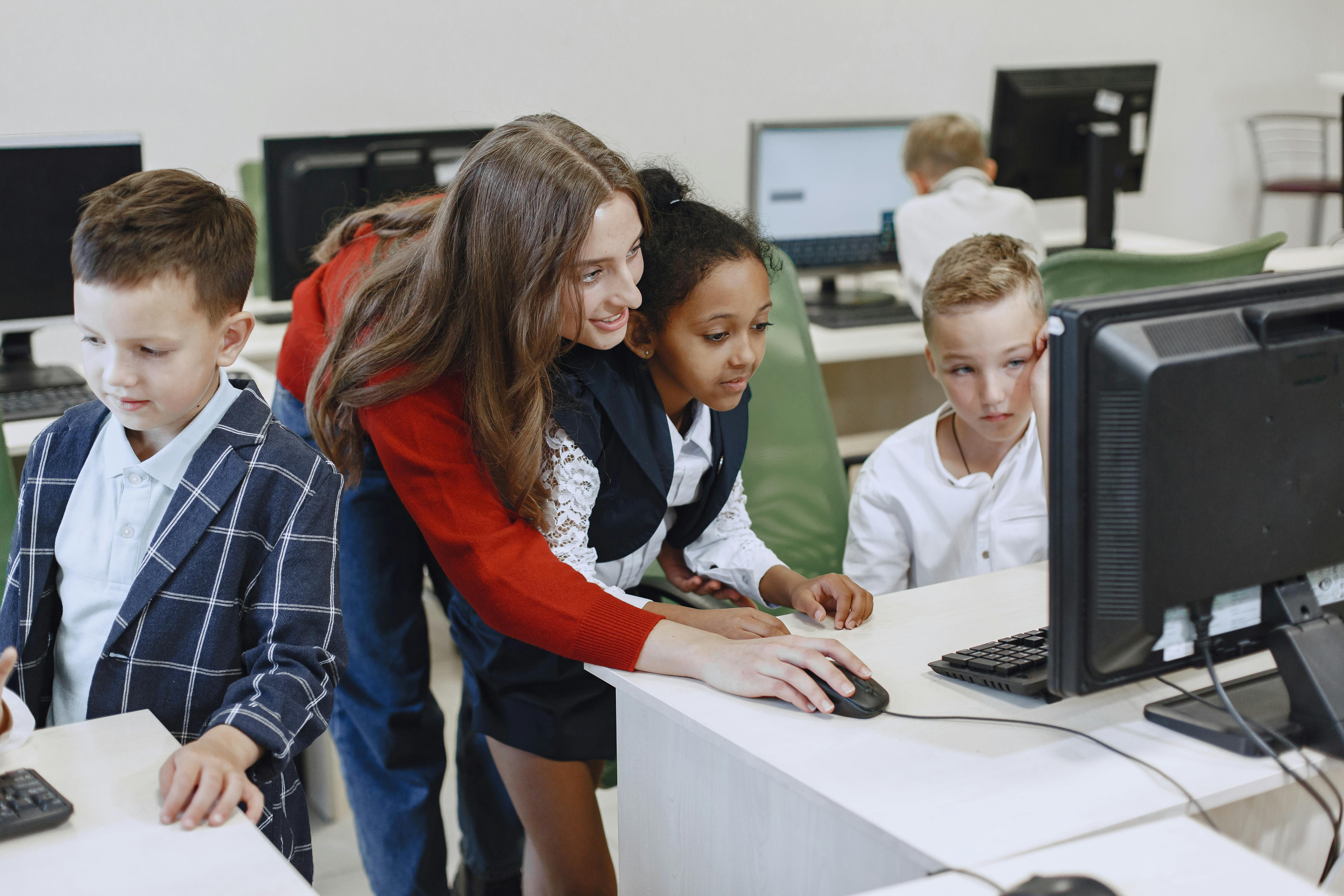 Teacher engaging with diverse children in a technology lesson using computers in a modern classroom