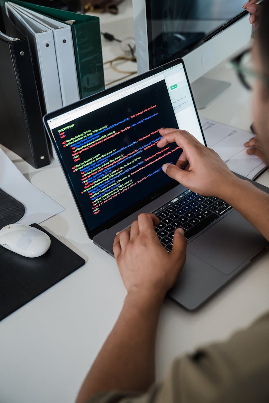 Close-up of a programmer pointing at code on a laptop during a debugging session.