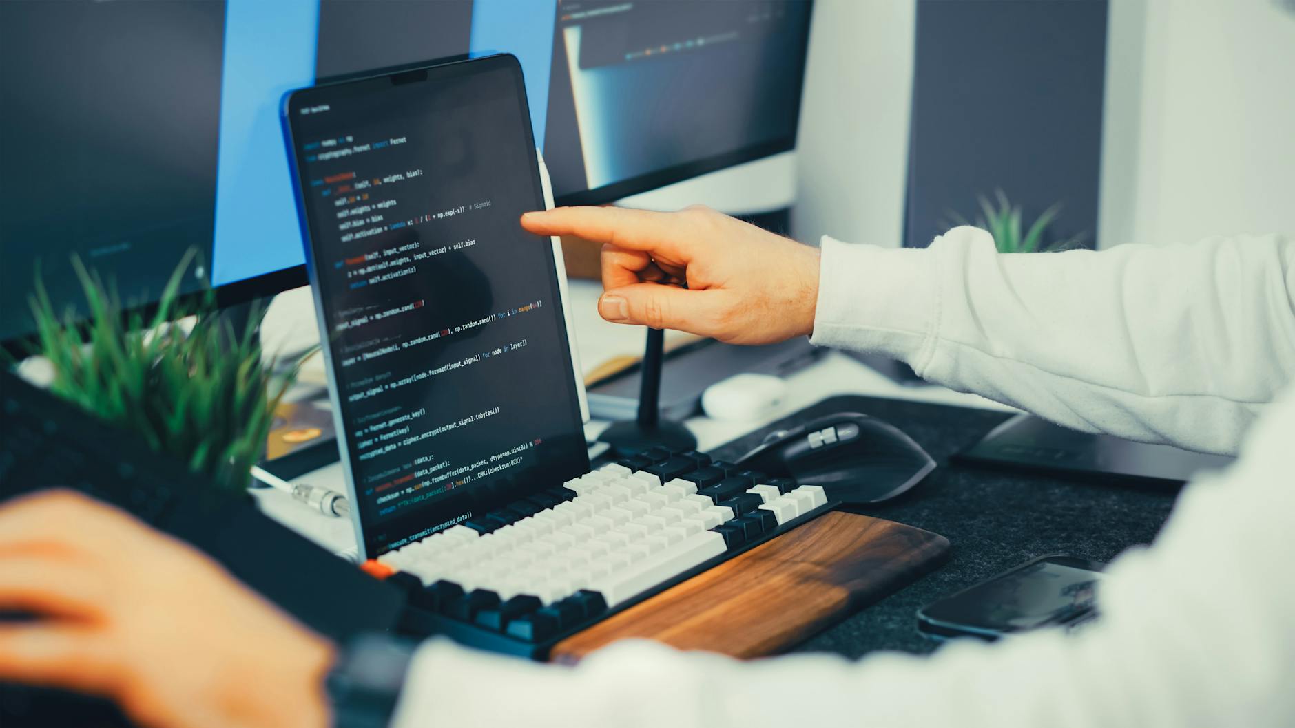 Developer reviewing code on a laptop and external monitor in an office as AI-written software increases security review work.