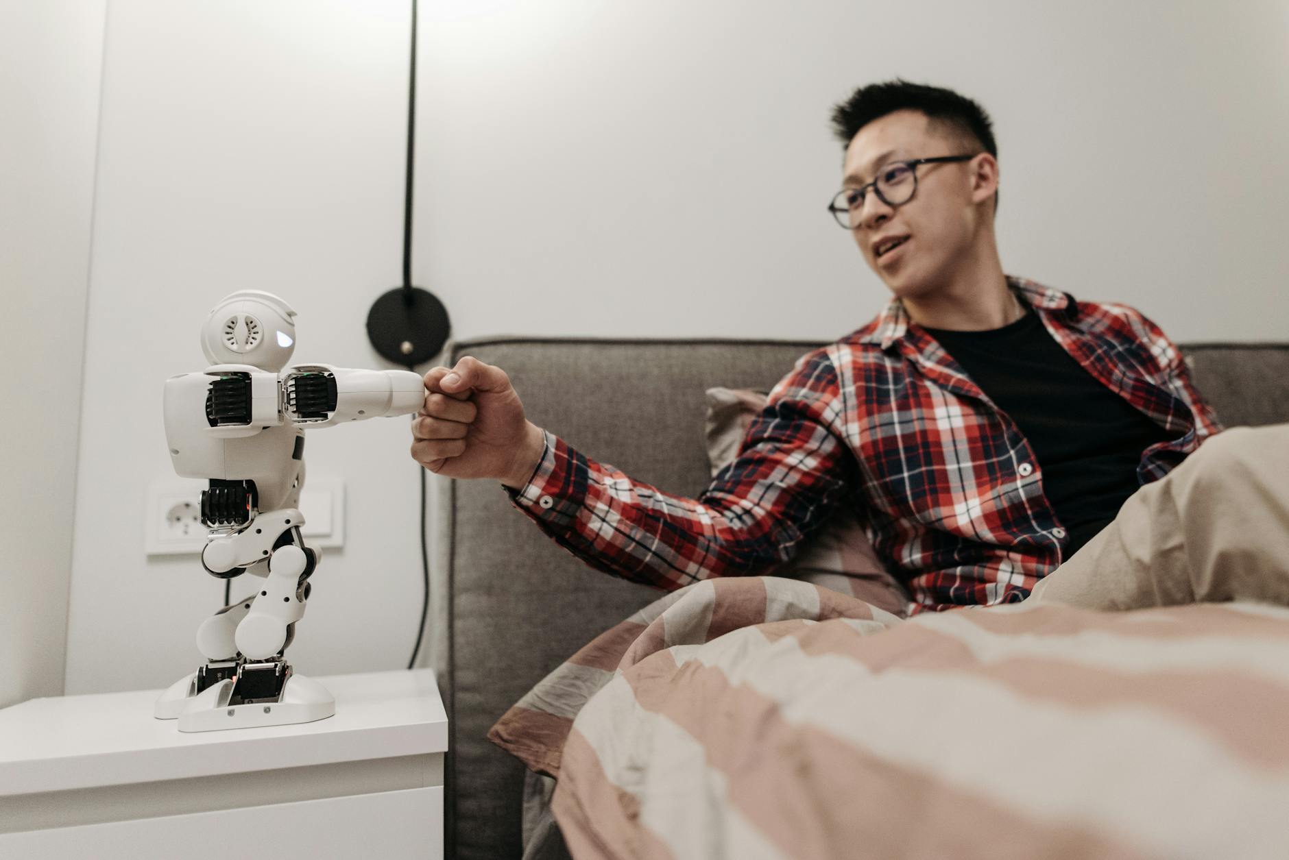 A person shakes hands with a small robot in a bedroom setting.