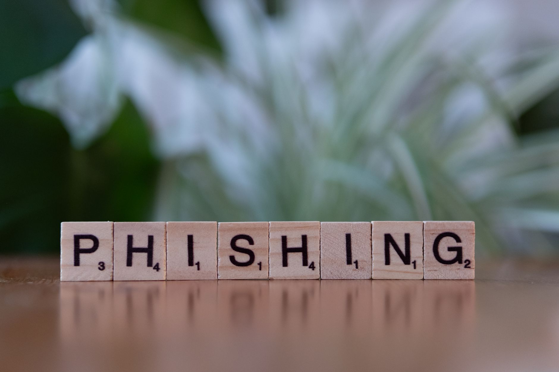 Wooden tiles spelling phishing on a desk, illustrating AI-assisted scam and cybersecurity risks